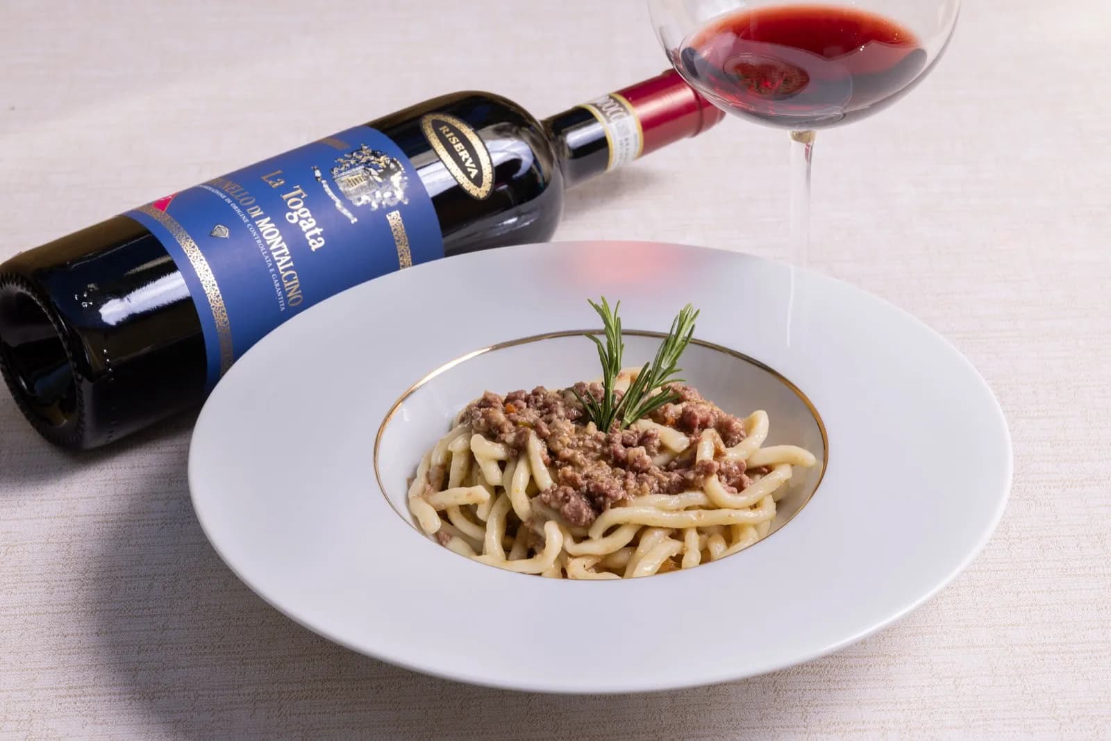 Pici con ragù e vino La Togata sulla tavola apparecchiata