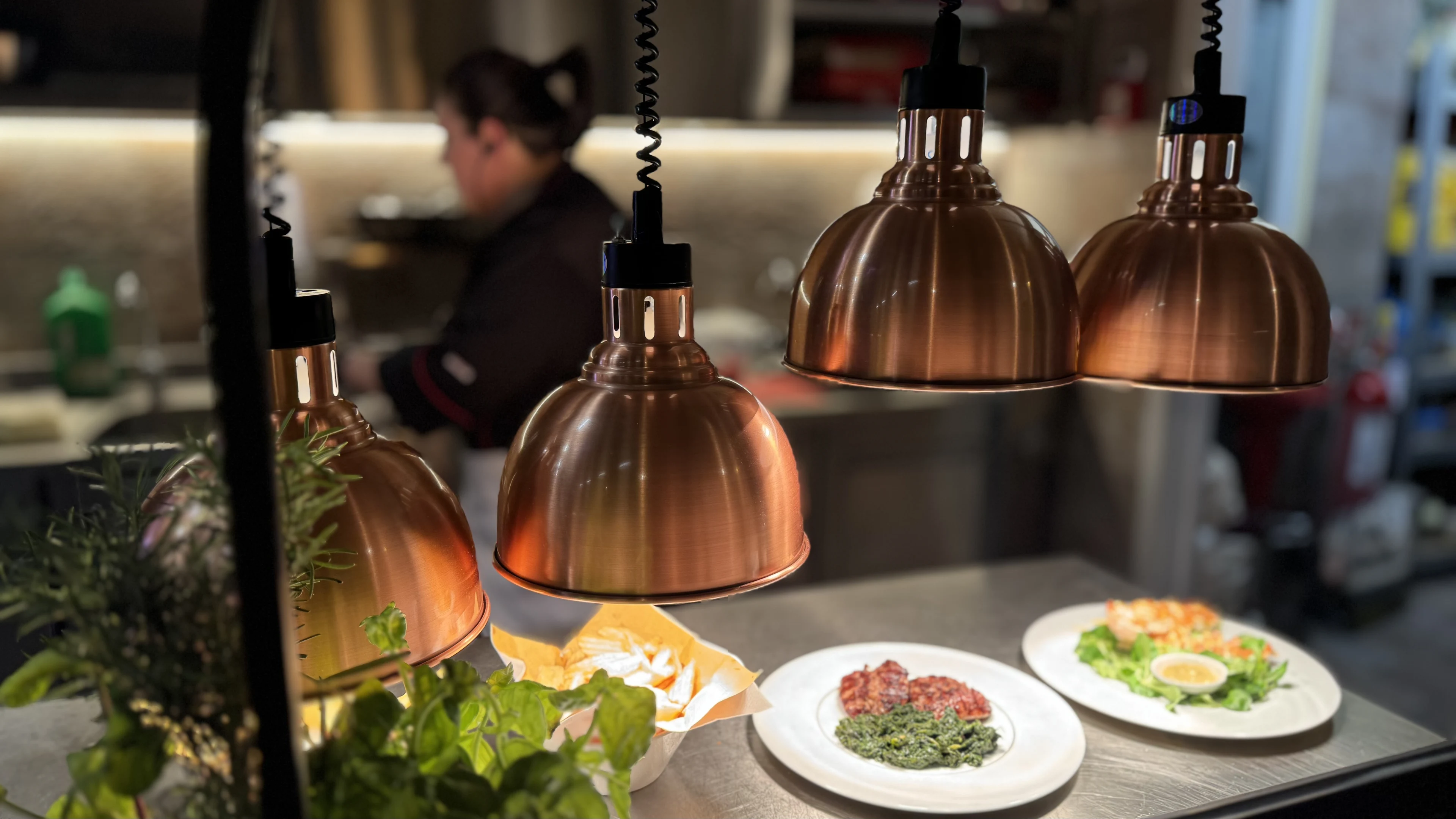 Copper heat lamps above finished dishes at the open-kitchen pass at Hosteria La Togata